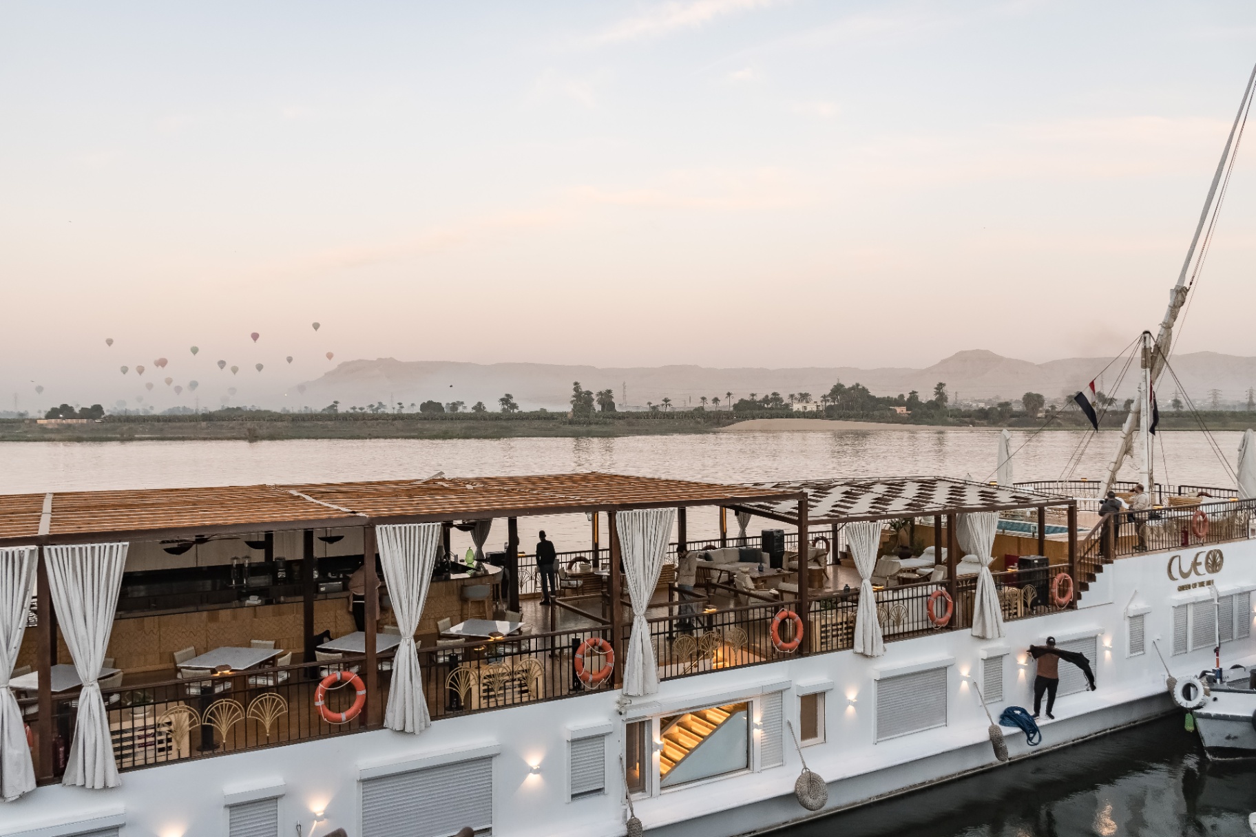 Sunrise view from Cleo Dahabiya's upper deck in Luxor, with hot-air balloons rising over the West Bank mountains across the Nile