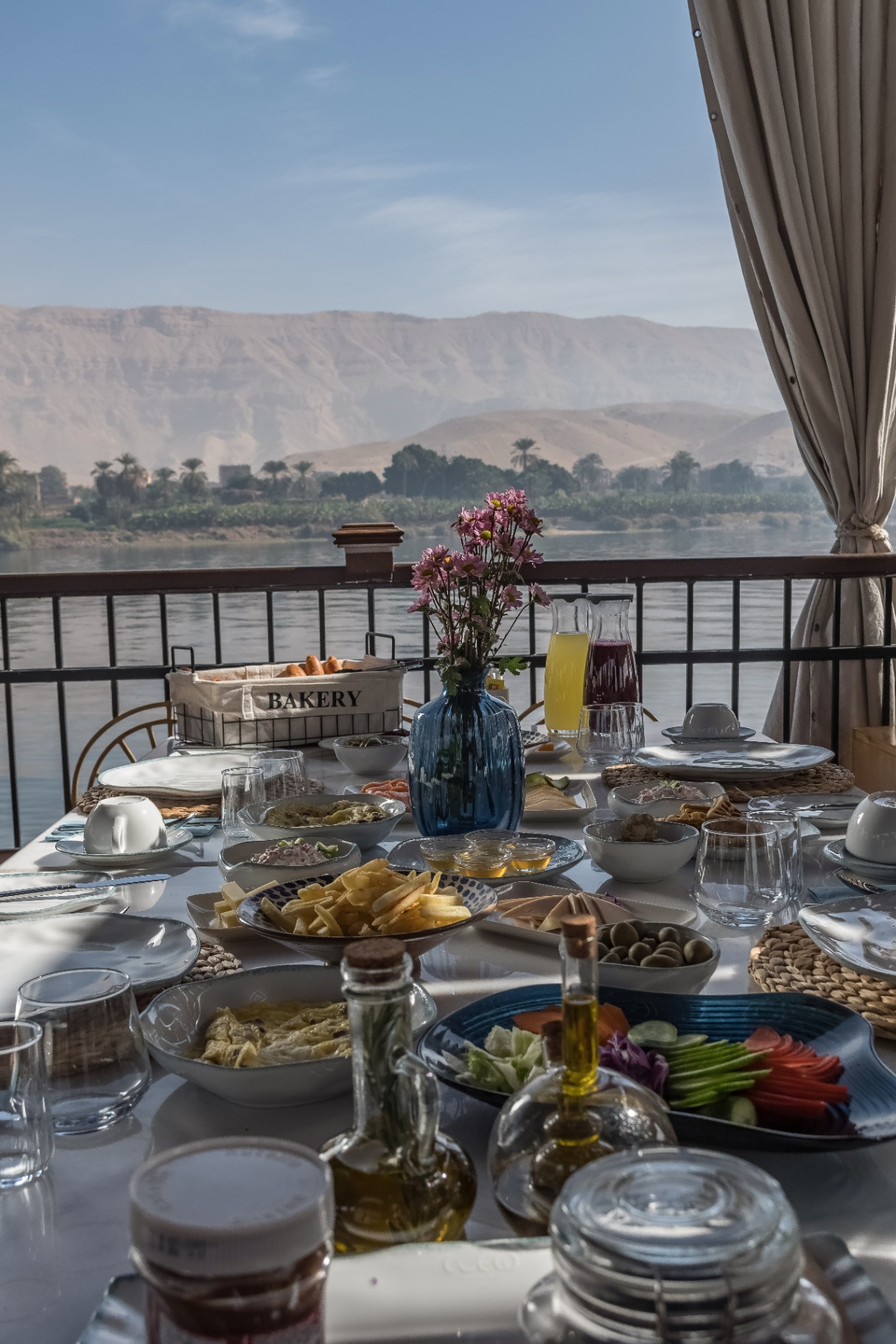 Riverside brunch table aboard Cleo Dahabiya with the desert mountains of Upper Egypt across the Nile