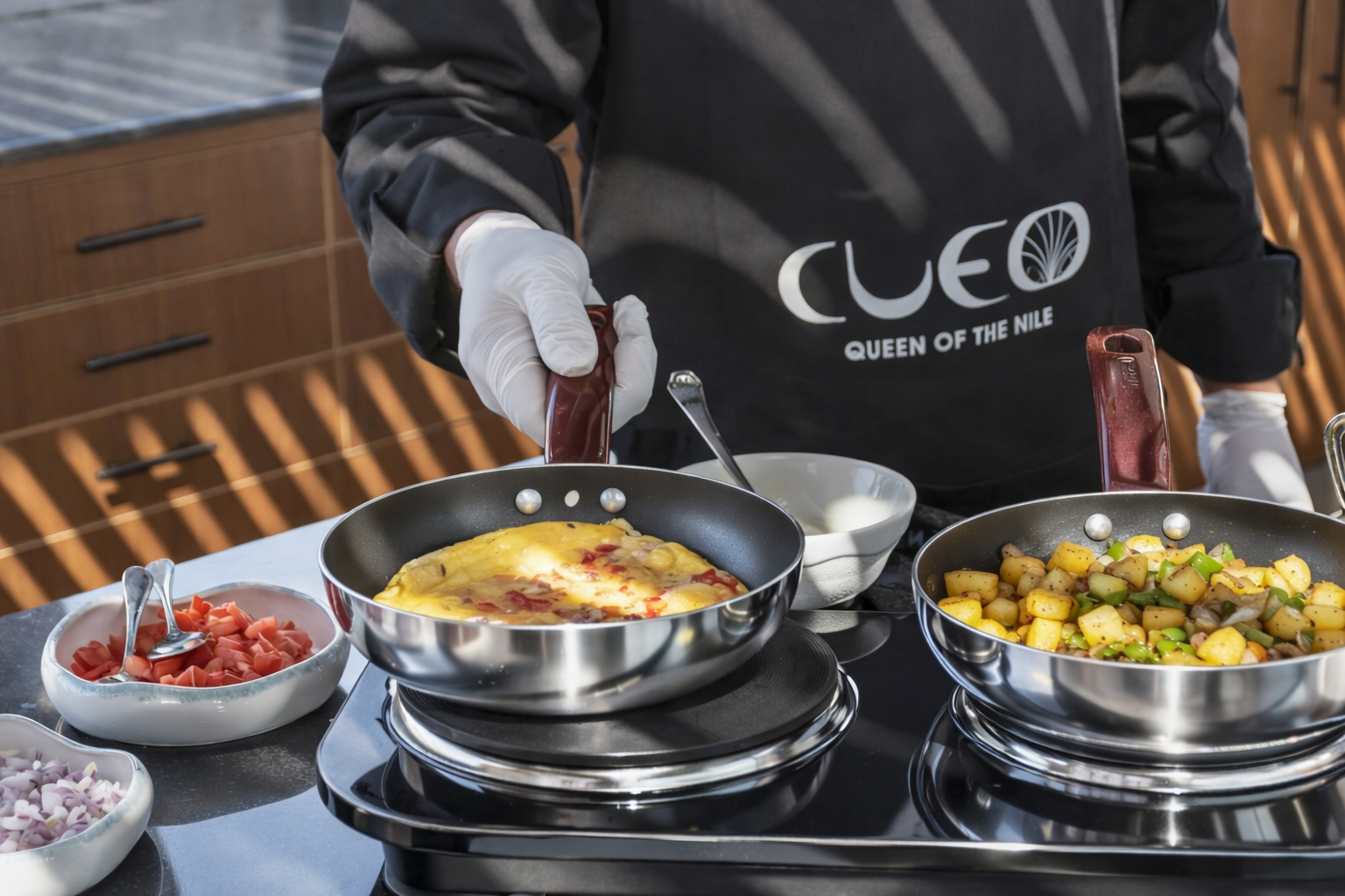 Chef in a Cleo Queen of the Nile apron preparing an omelette and sautéed potatoes on Cleo Dahabiya